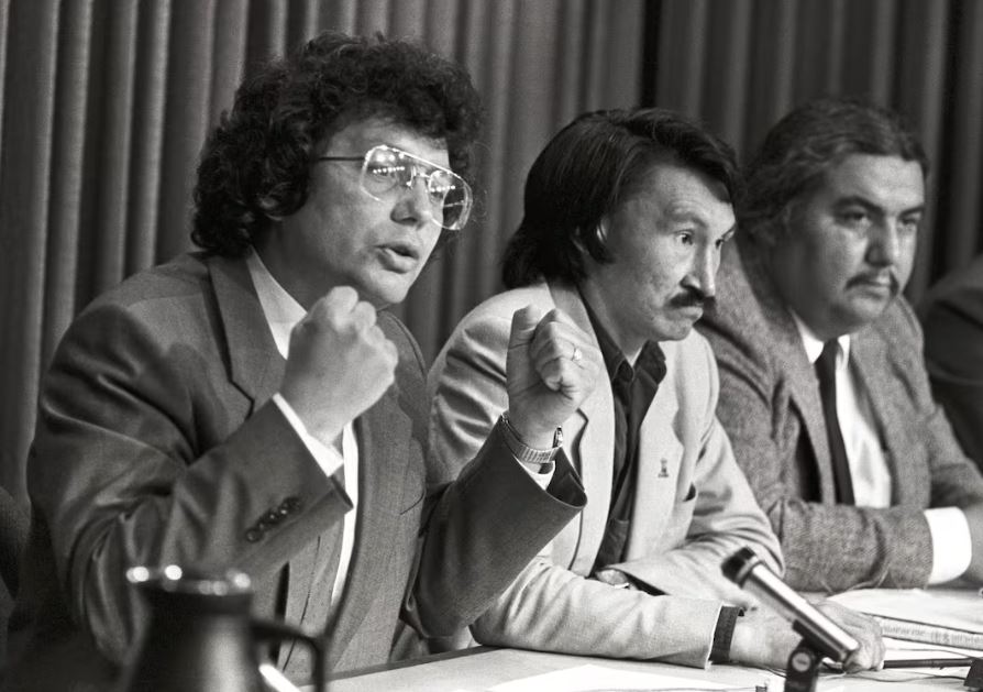 Three men speak at a press conference in a black and white photo.