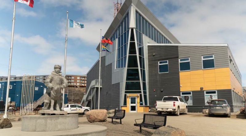 A building is seen with flags outside and a sculpture.