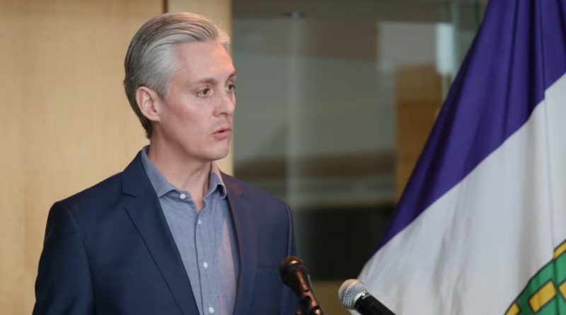 A man in a suit stands before 2 microphones, speaking.