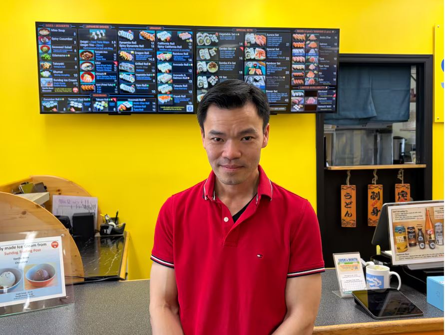 Sing Tu, owner of Sushi North stands infront of the counter with screens at the back.