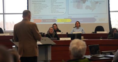 A man at a podium speaking to people at a bench.