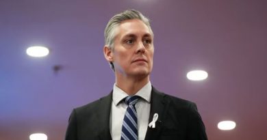 A man in a suite against a purple background looks to the right.