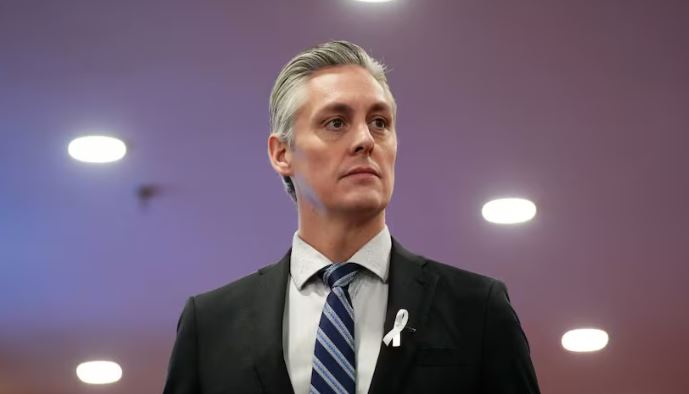 A man in a suite against a purple background looks to the right.