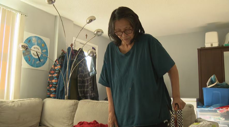 A woman with short hair and glasses standing with a cane.