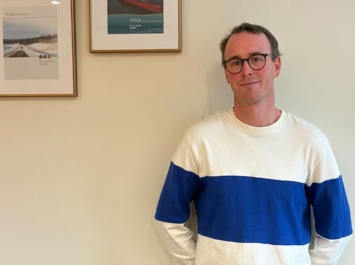 A man with short black hair wearing glasses and a blue and white horizontally-striped sweater