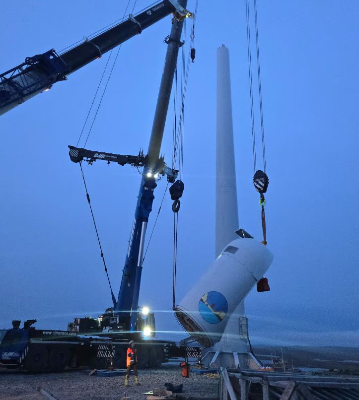 Two cranes lifting what looks like the top of the turbine into the air. The sky is blue, and it's either dusk or dawn.
