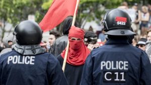 Un homme cagoulé fait face aux policiers qui ont mis en place un cordon de sécurité. Photo : Radio-Canada/Maxime Corneau