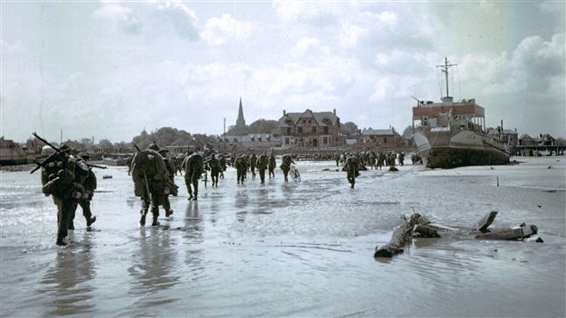Des soldats de l'infanterie canadienne débarquent sur la plage de Juno Beach et marchent en direction de Bernières-sur-Mer. Photo : Conseil régional de Basse-Normandie/Archives nationales du Canada