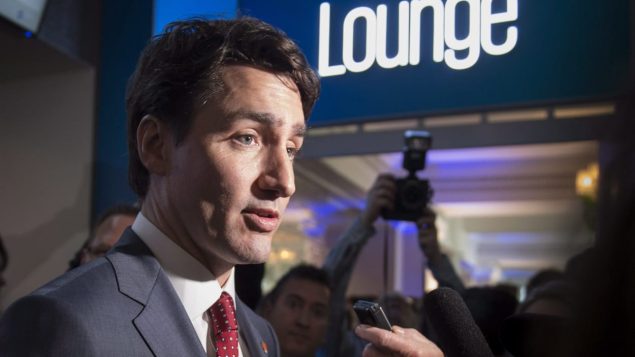 Justin Trudeau entouré de journalistes avec microphone et caméra.