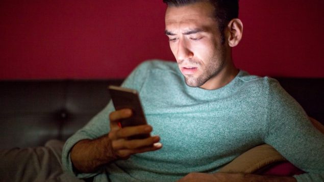 Un homme visiblement préoccupé ou tendu consulte son cellulaire durant la nuit. Photo : Radio-Canada