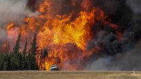 Smoke and flames from the wildfires erupt behind a car on the highway near Fort McMurray