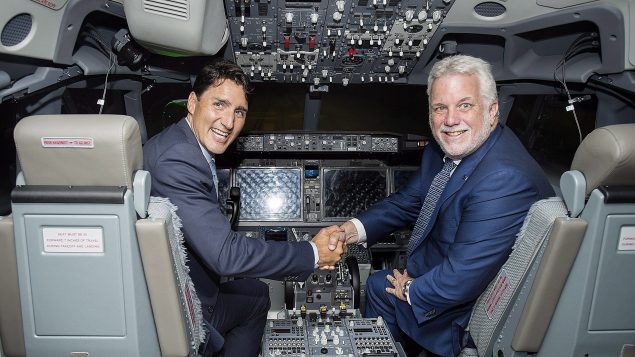 Le pm du Canada, Justin Trudeau, serre la main du pm du Québec, Philippe Couillard, dans un simulateur de vol fabriqué par CAE.