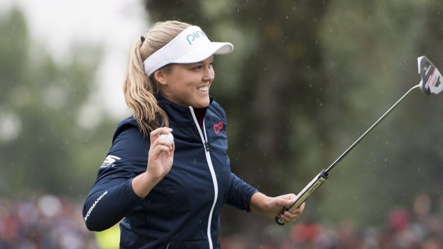 La golfeuse Brooke Henderson ramasse sa balle et célèbre sa victoire à l'Omnium canadien à Regina en Saskatchewan.