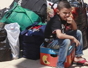 Un jeune garçon réfugié syrien est assis à côté de sacs à son arrivée au poste frontière de la ville irakienne de Qaim, à 320 kilomètres à l'ouest de Bagdad, en Irak. (Hadi Mizban / Associated Press)