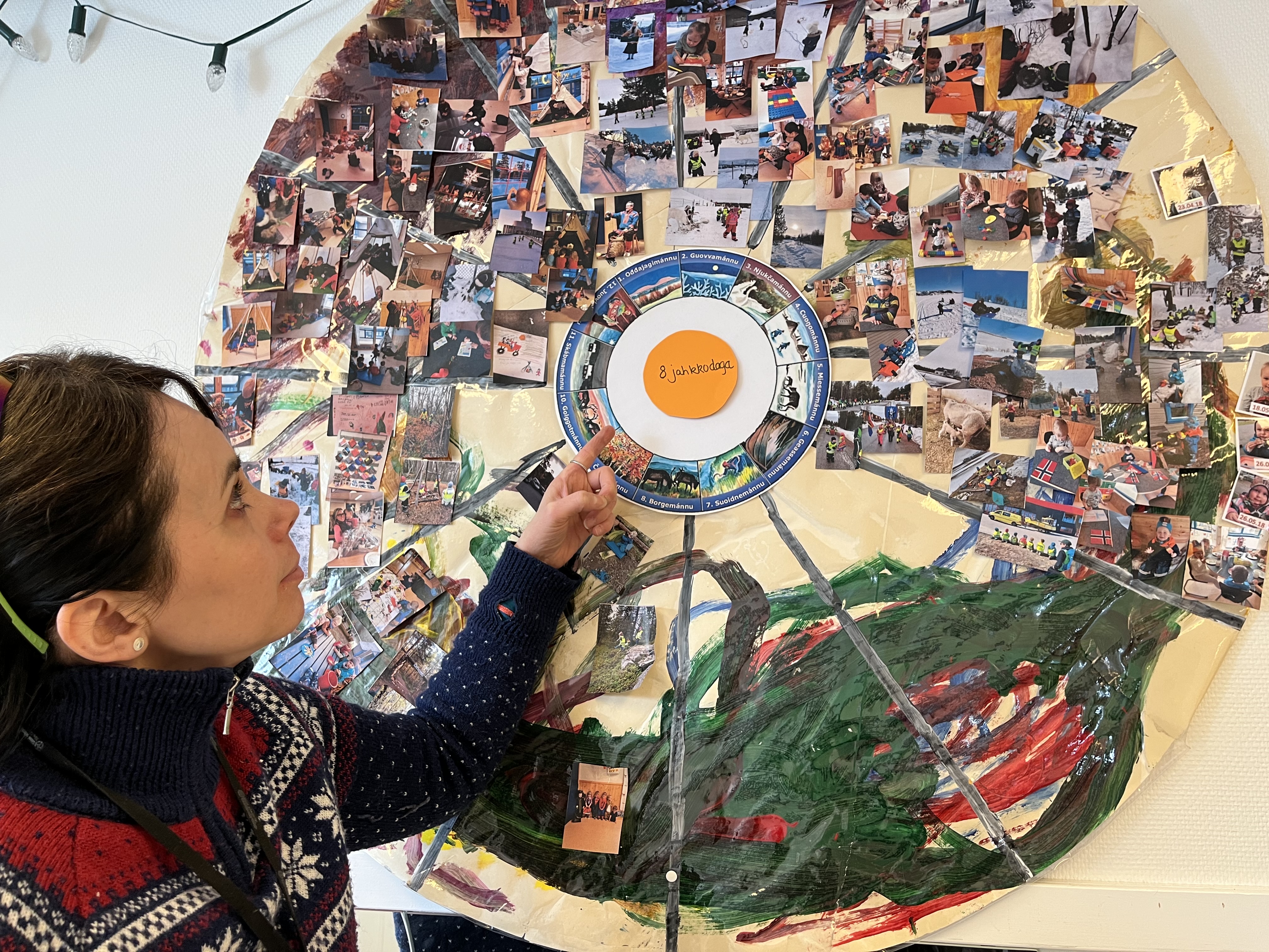 Karen Anne Marit Buljo, d’Altta Siida, pointe un calendrier mural sami où l’école affiche des images des activités des élèves au cours des différentes saisons. (Photo : Eilís Quinn, Regard sur l’Arctique)