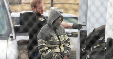 Une femme menottée au visage camouflé se tient à droite d'un agent de police.