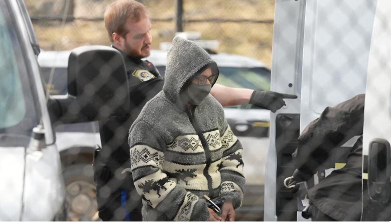 Une femme menottée au visage camouflé se tient à droite d'un agent de police.