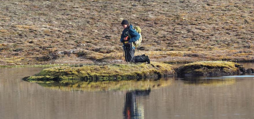 Une jeune chercheuse est agenouillée sur la toundra pour récolter des échantillons.