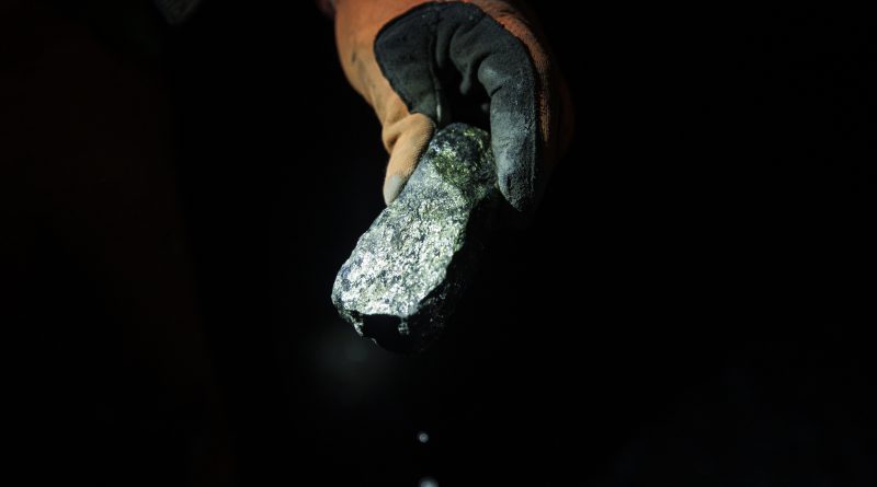 Une main tient un morceau de minerai dans l'obscurité