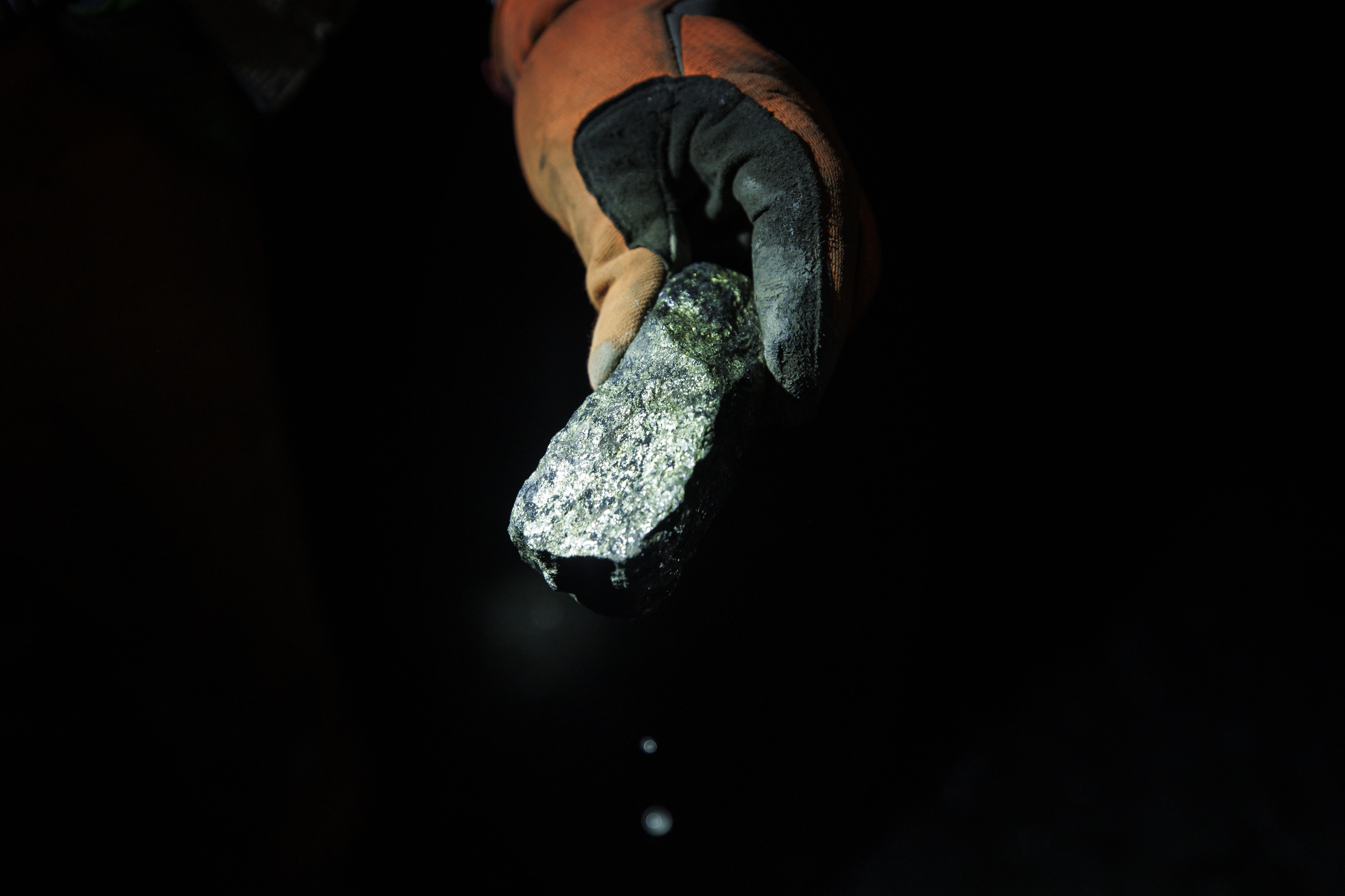 Une main tient un morceau de minerai dans l'obscurité