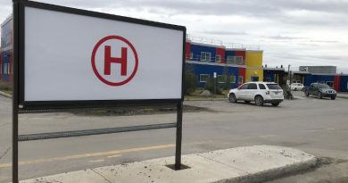 Devant un édifice, image d'une affiche ayant un « H » en lettre majuscule enouré d'un cercle