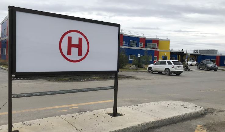 Devant un édifice, image d'une affiche ayant un « H » en lettre majuscule enouré d'un cercle