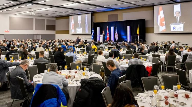 Des gens assis autour de tables dans une grande salle de conférence en 2023.