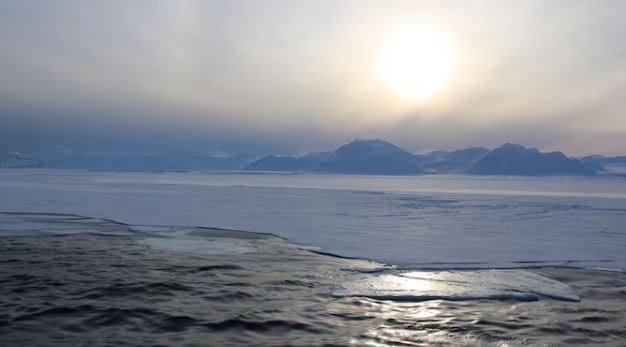 Vue de l'eau qui semble glacée devant des montagnes.
