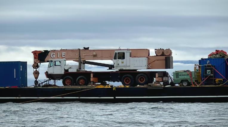 Un camion-remorque et un conteneur maritime sont posés sur une barge qui flotte sur l'eau, près d'Iqaluit, le 19 septembre 2024.