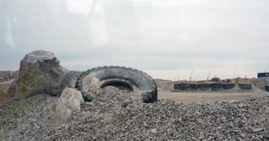 Un pneu traîne dans du gravier, près d'installations entourées d'une clôture, en août 2024.