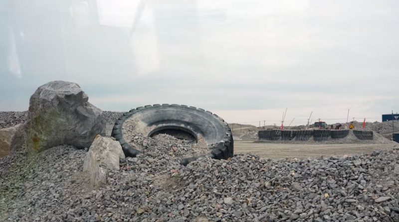 Un pneu traîne dans du gravier, près d'installations entourées d'une clôture, en août 2024.