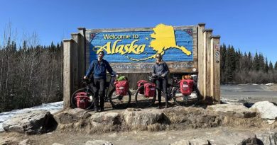 Nicolas Roulx et Catherine Chagnon posent avec leurs vélos devant une grande enseigne «Welcome to Alaska».