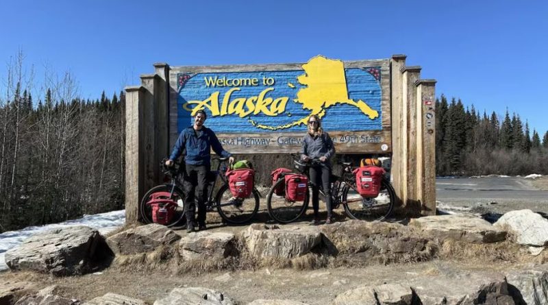 Nicolas Roulx et Catherine Chagnon posent avec leurs vélos devant une grande enseigne «Welcome to Alaska».
