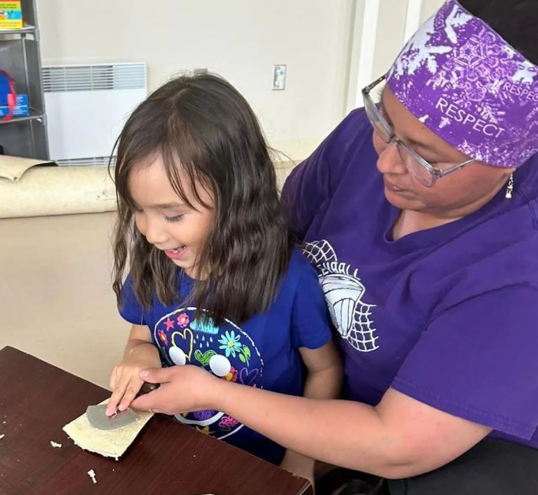 Une femme montre à une fillette comment utiliser un « ulu », un outil traditionnel inuit.