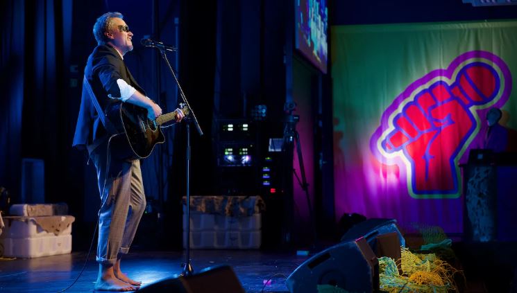 Un chanteur dont les yeux sont peints en noir chante dans un micro en jouant de la guitare sur la scène du Centre culturel Katuaq, à Nuuk, au Groenland.