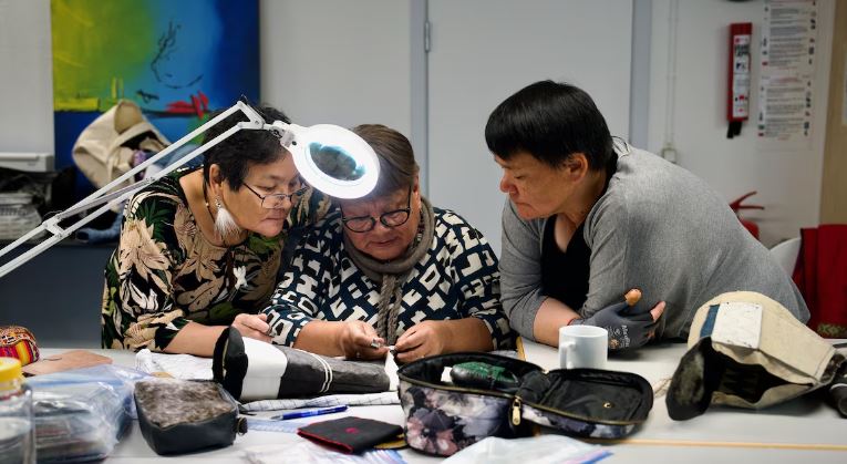 Deux femmes regardent attentivement les techniques de confection de chaussons traditionnels inuit d'une couturière, lors d'un atelier à Nuuk, au Groenland, le 10 octobre 2024.