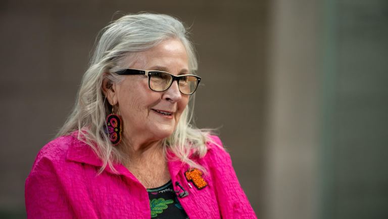 Marie Wilson porte une veste rose, des boucles d'oreilles perlées et une broche symbolisant un chandail orange pour la journée de commémoration des survivants de pensionnats pour Autochtones.