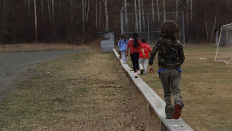 Des enfants de dos qui marchent en équilibre sur un muret.