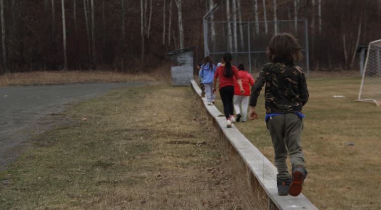 Des enfants de dos qui marchent en équilibre sur un muret.
