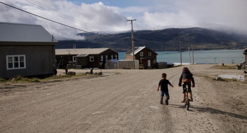 Une jeune fille fait de la bicyclette et un garçon court à côté d'elle dans une rue de Pangnirtung, en août 2023.