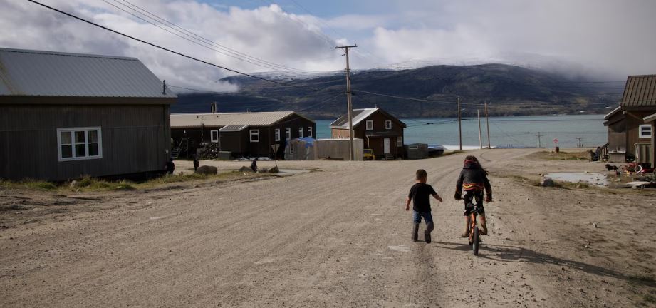 Une jeune fille fait de la bicyclette et un garçon court à côté d'elle dans une rue de Pangnirtung, en août 2023.