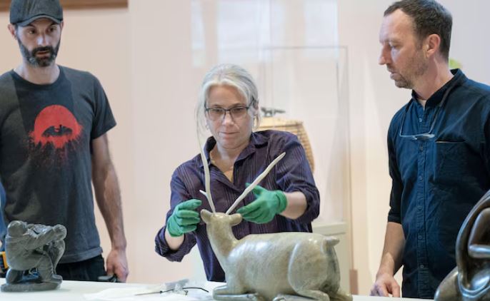 Une femme et deux hommes installent une sculpture.