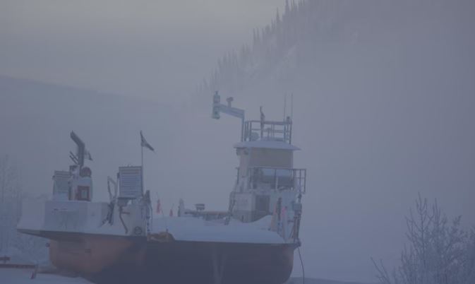 Un navire repose hors de l'eau au pied d'une montagne, dans le brouillard.