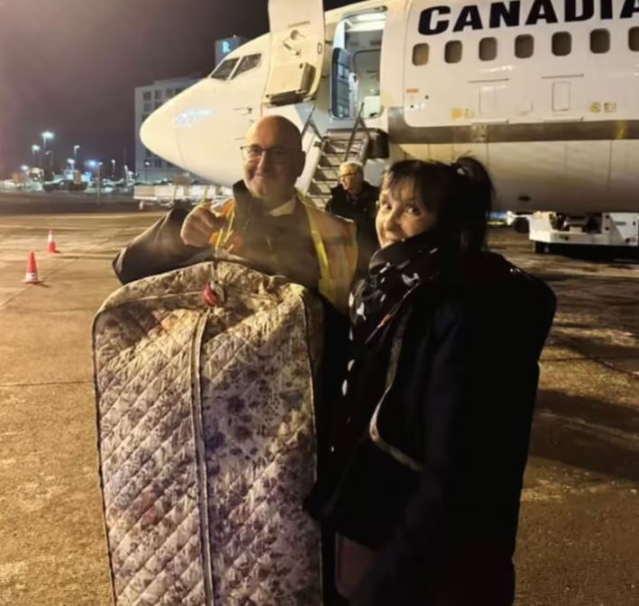 Richard de Aguayo tient une house de vêtement devant un avion, une agente de bord est à ses côtés.