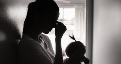 Silhouette d'une femme qui a son jeune enfant dans les bras, adossée contre le mur, dans un couloir. Elle se touche le front comme si elle avait mal à la tête.