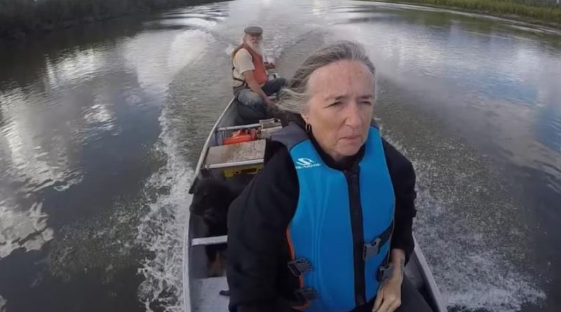 Une femme est à l'avant d'une pirogue, alors qu'un homme est à la barre.