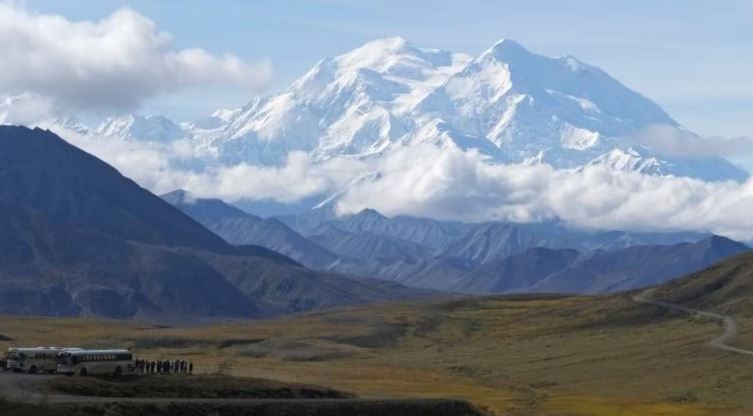 Des touristes à côté d'autocar regardent la montagne.