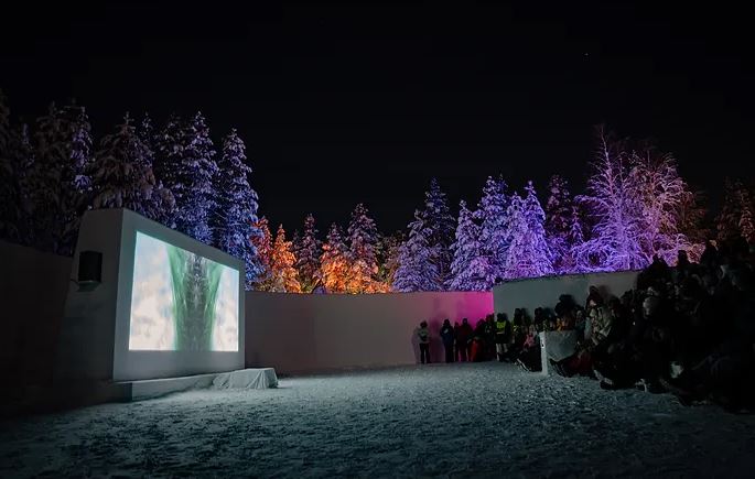 Des gens sont rassemblés devant une projection et des arbres colorés.