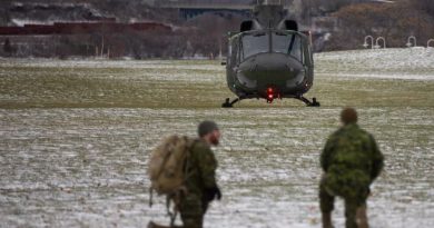 Deux membres militaire accroupis avec au loin l'hélicoptère CH-146 Griffon de l'Aviation royale canadienne.