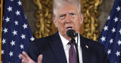 Donald Trump au micro, devant des drapeaux américains, bouge la main en parlant.